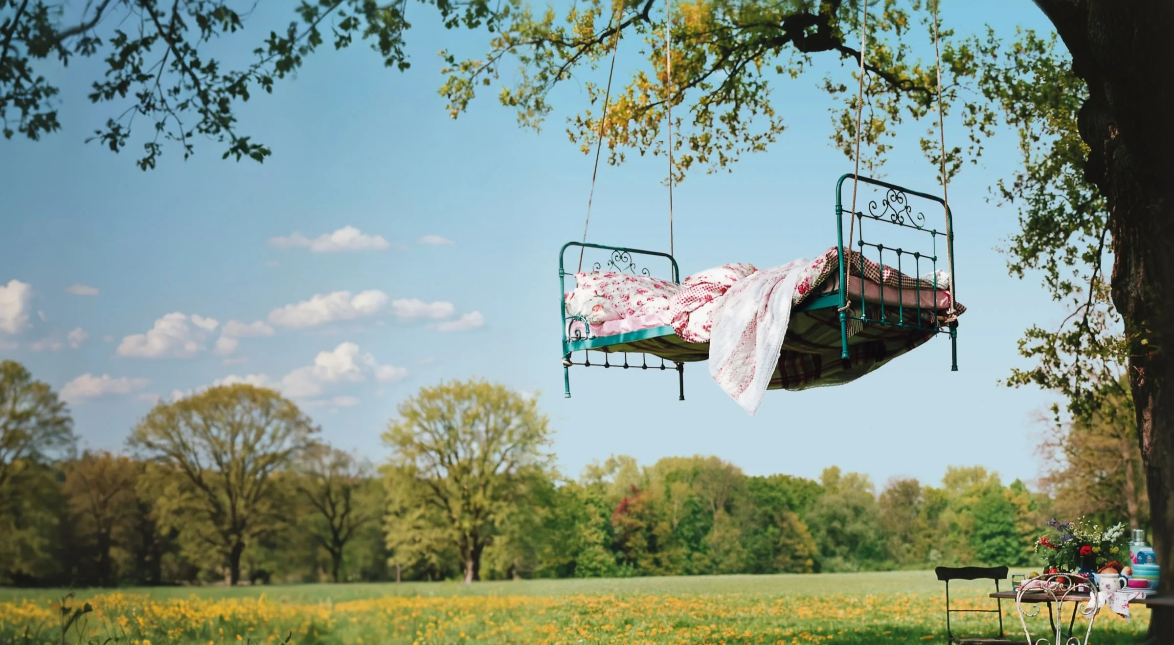 Ein an einem alten Baum aufgehängtes Bett über einer blühenden Wiese
